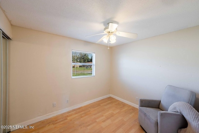 living area with light wood-type flooring, ceiling fan, a textured ceiling, and baseboards