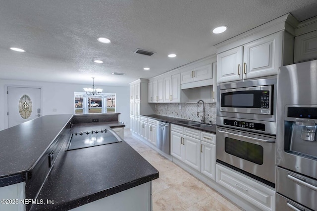 kitchen with stainless steel appliances, dark countertops, visible vents, white cabinetry, and a sink