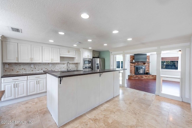 kitchen featuring a breakfast bar area, stainless steel appliances, dark countertops, white cabinets, and a kitchen island