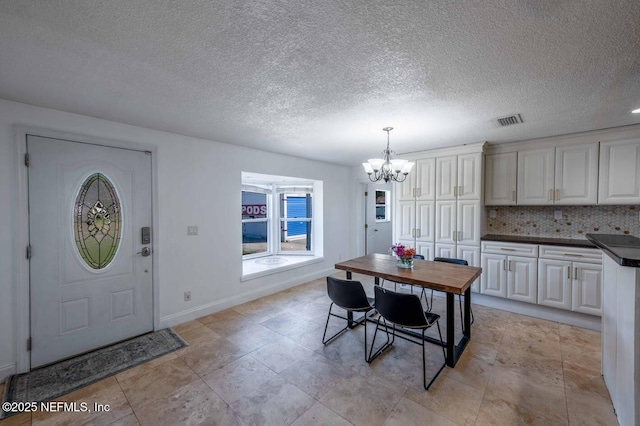 interior space featuring baseboards, visible vents, a chandelier, and a textured ceiling