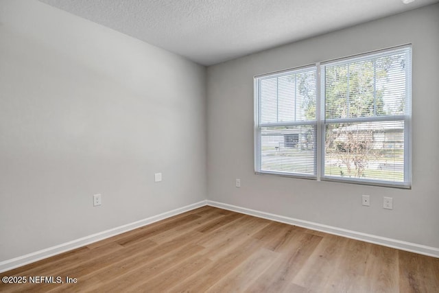 unfurnished room with a textured ceiling, light wood finished floors, and baseboards