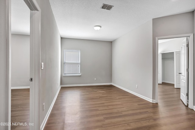 unfurnished bedroom with a textured ceiling, dark wood-style flooring, visible vents, baseboards, and a spacious closet