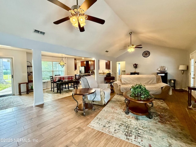 living area featuring visible vents, baseboards, lofted ceiling, ceiling fan, and light wood-style floors