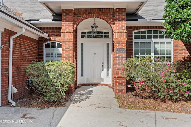 entrance to property featuring roof with shingles and brick siding