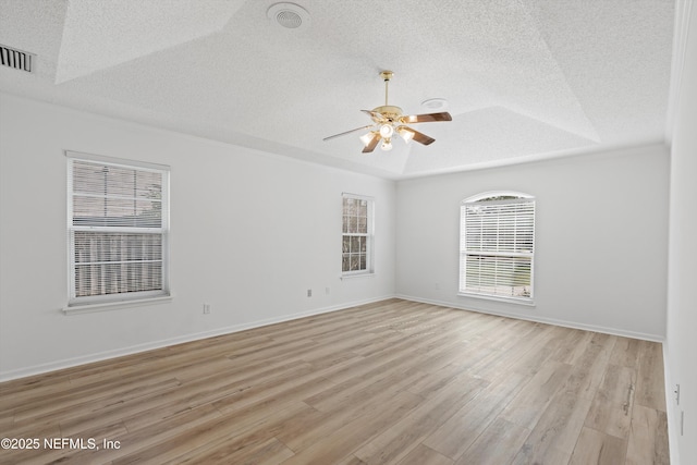 empty room with light wood-style floors, visible vents, a raised ceiling, and a textured ceiling