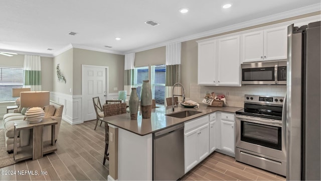 kitchen featuring appliances with stainless steel finishes, wood tiled floor, white cabinetry, a sink, and a peninsula