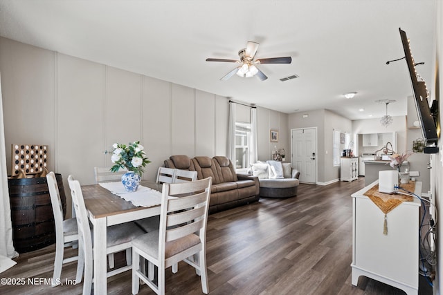 dining space featuring dark wood-type flooring, visible vents, a decorative wall, and ceiling fan