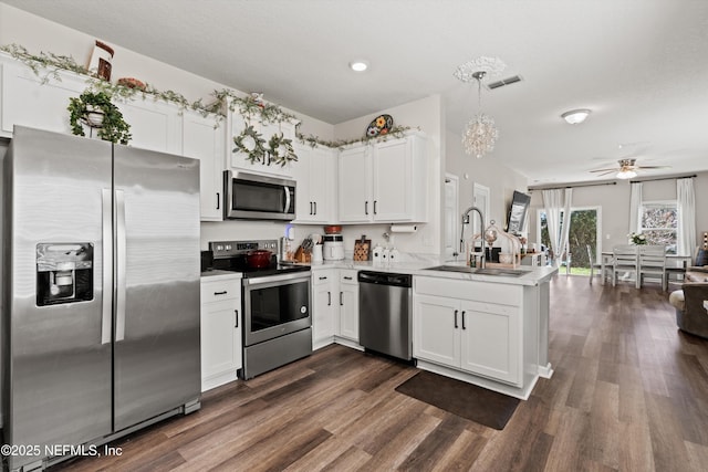 kitchen with appliances with stainless steel finishes, a peninsula, light countertops, white cabinetry, and a sink