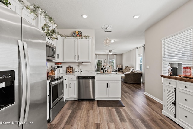 kitchen with a peninsula, a sink, white cabinetry, open floor plan, and appliances with stainless steel finishes