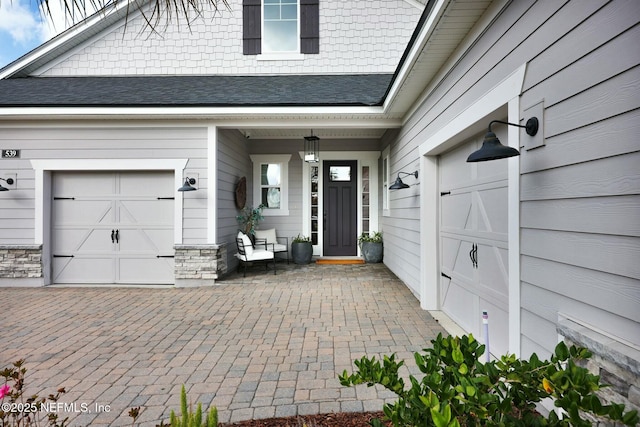 property entrance featuring an attached garage, decorative driveway, and roof with shingles