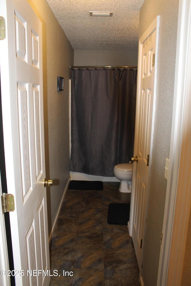 full bath featuring baseboards, a textured wall, a textured ceiling, and toilet