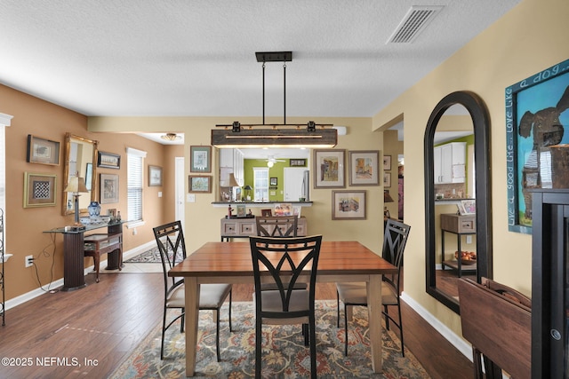 dining area featuring a textured ceiling, dark wood-style flooring, visible vents, and baseboards