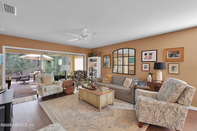 living area featuring visible vents, ceiling fan, a textured ceiling, and wood finished floors