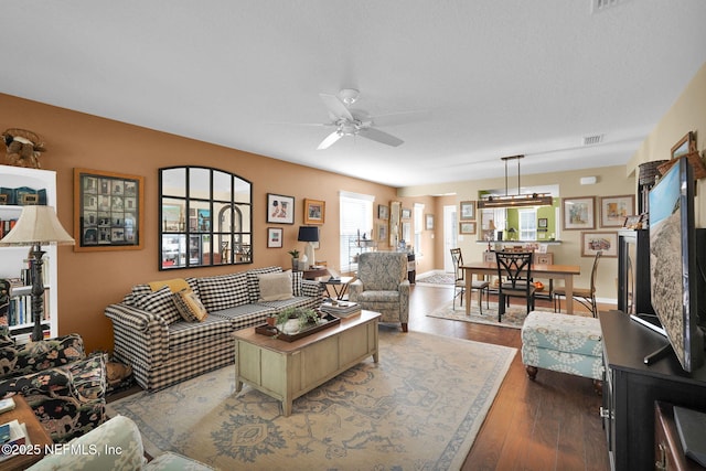 living room featuring dark wood-style floors, ceiling fan, and visible vents