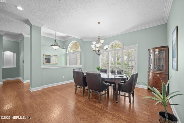 dining room with baseboards, ornamental molding, wood finished floors, a textured ceiling, and a chandelier