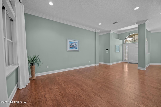 interior space featuring a textured ceiling, ornamental molding, wood finished floors, and baseboards