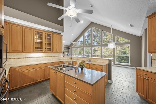 kitchen with stone tile floors, a kitchen island, a peninsula, black electric cooktop, and a sink