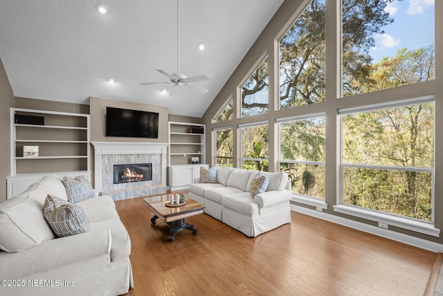 living room featuring a textured ceiling, high vaulted ceiling, built in shelves, a premium fireplace, and wood finished floors