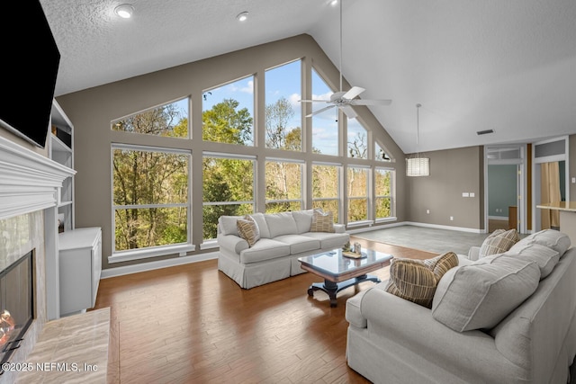 living room featuring light wood-type flooring, a healthy amount of sunlight, high vaulted ceiling, and a high end fireplace