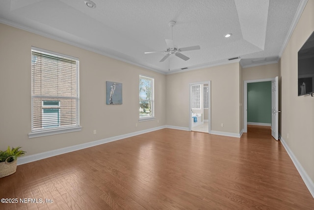 empty room with baseboards, wood finished floors, a raised ceiling, and crown molding