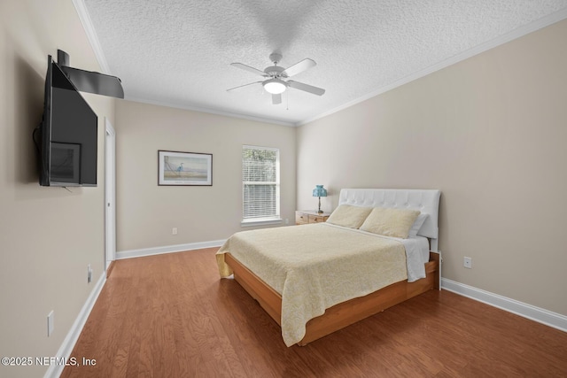 bedroom featuring a textured ceiling, baseboards, wood finished floors, and crown molding