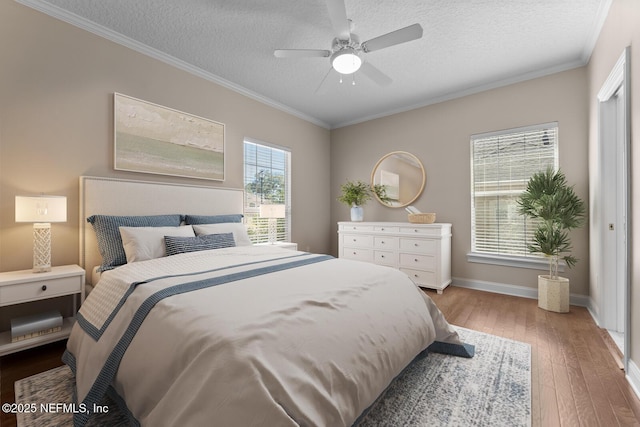 bedroom with a textured ceiling, a ceiling fan, baseboards, ornamental molding, and wood-type flooring