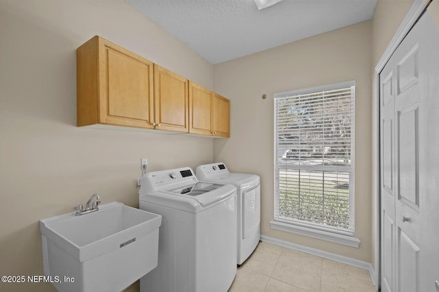 laundry area featuring cabinet space, baseboards, washing machine and dryer, a sink, and light tile patterned flooring