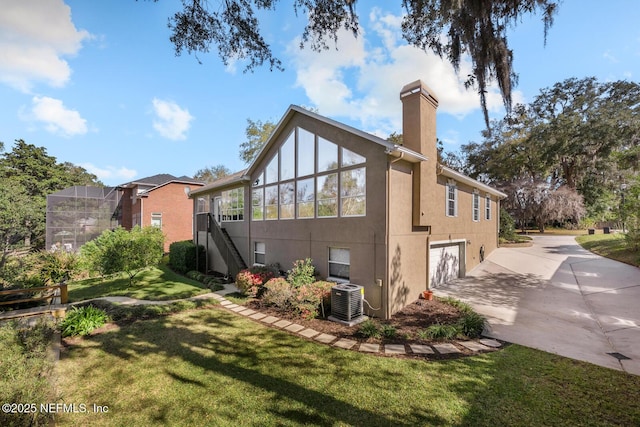 rear view of house with a chimney, central air condition unit, concrete driveway, a lawn, and a garage