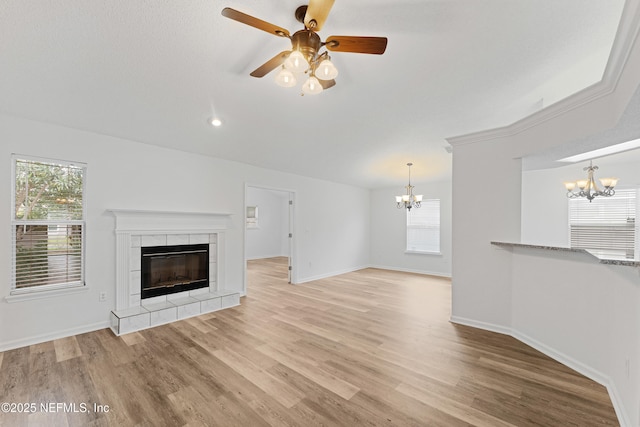 unfurnished living room featuring baseboards, a tiled fireplace, a wealth of natural light, and light wood-style floors