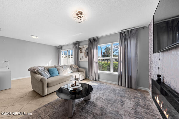 living area with a textured ceiling, light tile patterned floors, a glass covered fireplace, and baseboards