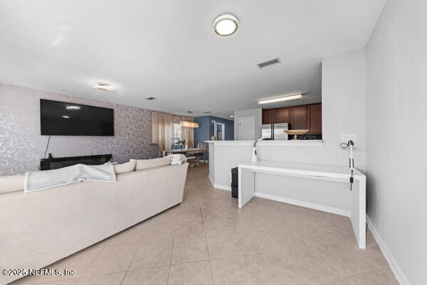 living area featuring light tile patterned floors, visible vents, an accent wall, baseboards, and wallpapered walls