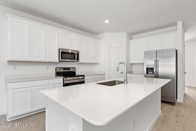 kitchen with appliances with stainless steel finishes, white cabinetry, a sink, and an island with sink