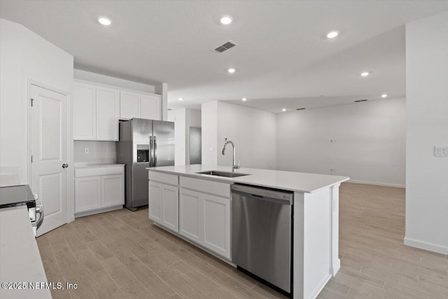 kitchen with an island with sink, appliances with stainless steel finishes, light countertops, white cabinetry, and a sink