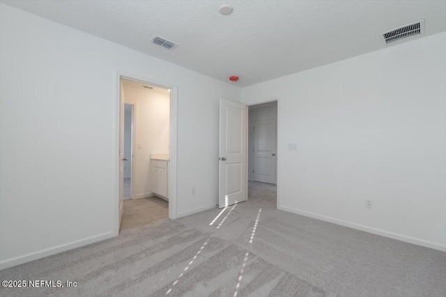 unfurnished bedroom featuring baseboards, visible vents, a textured ceiling, and light colored carpet