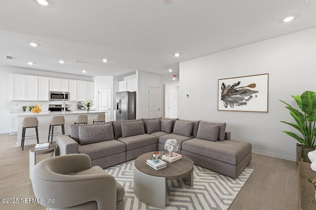 living area with light wood-style floors, recessed lighting, visible vents, and baseboards