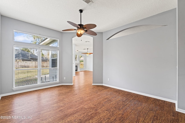 unfurnished room with a textured ceiling, wood-type flooring, a fireplace, and baseboards