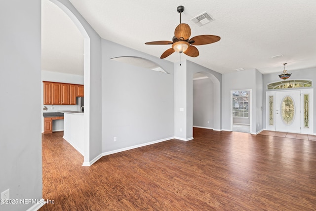 unfurnished living room with a textured ceiling, wood finished floors, visible vents, baseboards, and a ceiling fan