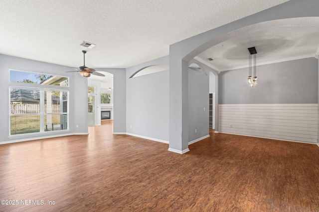 unfurnished room featuring a textured ceiling, ceiling fan, arched walkways, wood finished floors, and a glass covered fireplace