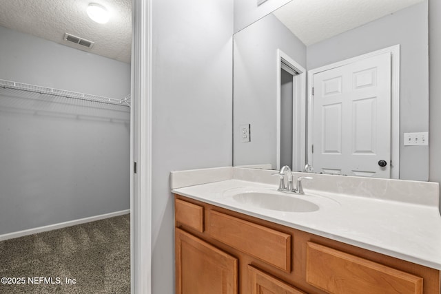 bathroom featuring baseboards, visible vents, a textured ceiling, and vanity