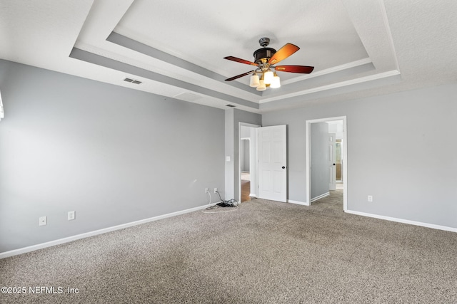 unfurnished bedroom with carpet floors, a tray ceiling, visible vents, ornamental molding, and baseboards