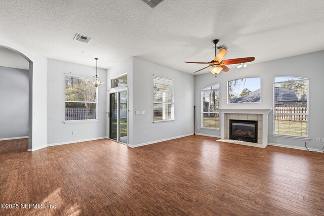 unfurnished living room with visible vents, arched walkways, wood finished floors, a fireplace, and ceiling fan with notable chandelier