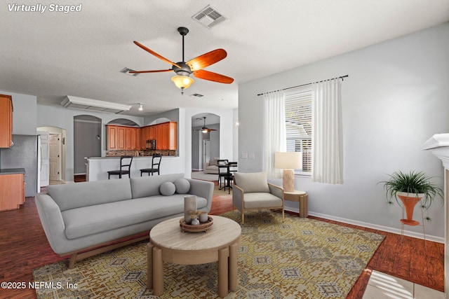 living area with arched walkways, visible vents, ceiling fan, wood finished floors, and baseboards