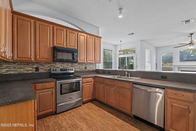 kitchen with appliances with stainless steel finishes, dark countertops, a sink, and visible vents