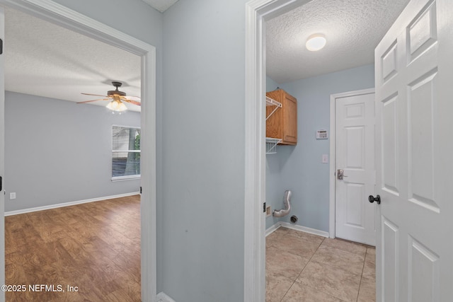 clothes washing area with a textured ceiling, ceiling fan, cabinet space, and baseboards