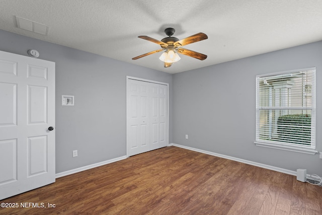 unfurnished bedroom featuring visible vents, a textured ceiling, baseboards, and wood finished floors