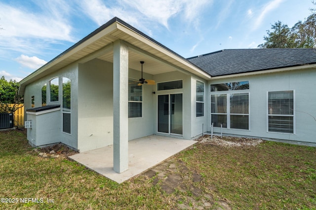 rear view of property featuring a ceiling fan, a yard, roof with shingles, stucco siding, and a patio area