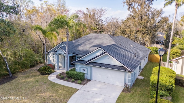 view of front of home with stucco siding, concrete driveway, fence, a garage, and a front lawn