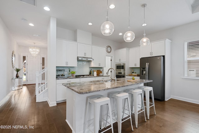 kitchen with white cabinets, appliances with stainless steel finishes, a sink, under cabinet range hood, and backsplash