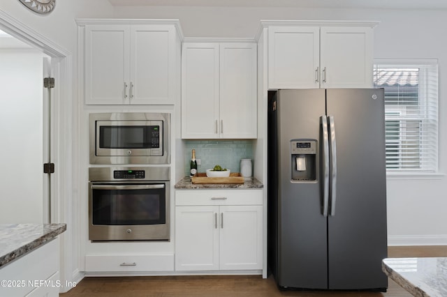 kitchen featuring white cabinets, wood finished floors, light stone countertops, stainless steel appliances, and backsplash