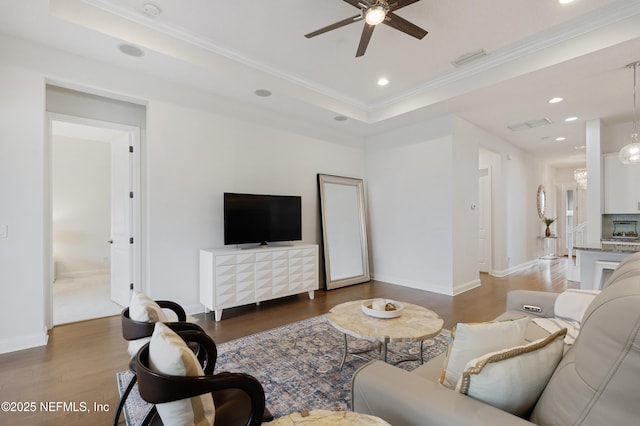 living room featuring ceiling fan, recessed lighting, wood finished floors, ornamental molding, and a tray ceiling